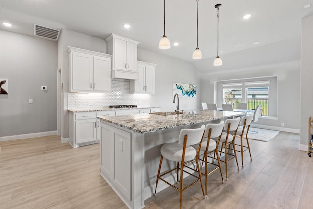 kitchen with a kitchen island with sink, sink, white cabinets, and decorative light fixtures