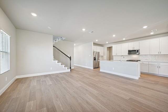 kitchen with a center island with sink, light wood-type flooring, white cabinetry, and stainless steel appliances