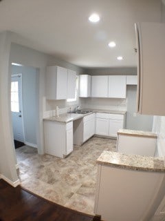 kitchen with light stone countertops, sink, white cabinets, and light wood-type flooring