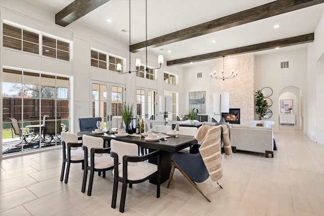 tiled dining area with beamed ceiling, a high ceiling, a chandelier, and a stone fireplace