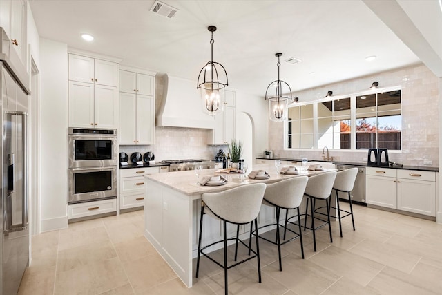 kitchen with appliances with stainless steel finishes, backsplash, decorative light fixtures, white cabinets, and a center island