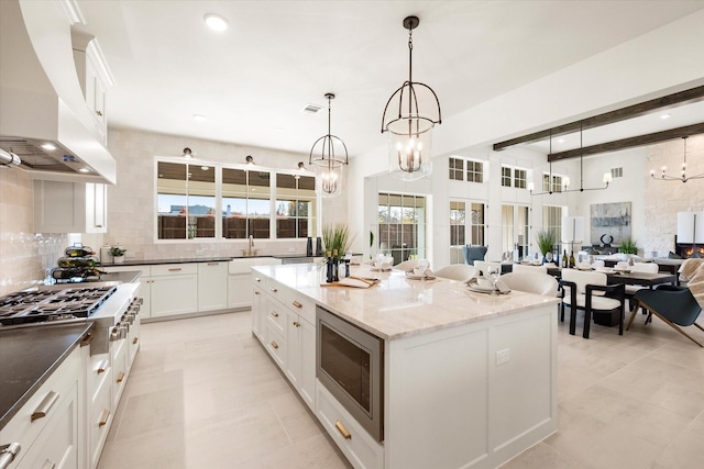 kitchen featuring custom exhaust hood, appliances with stainless steel finishes, tasteful backsplash, decorative light fixtures, and a kitchen island