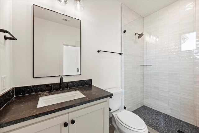 bathroom with tiled shower, vanity, and toilet