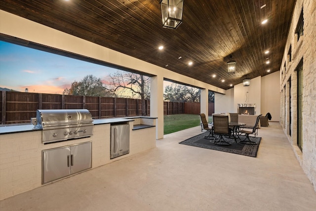 patio terrace at dusk featuring area for grilling, an outdoor fireplace, and a grill