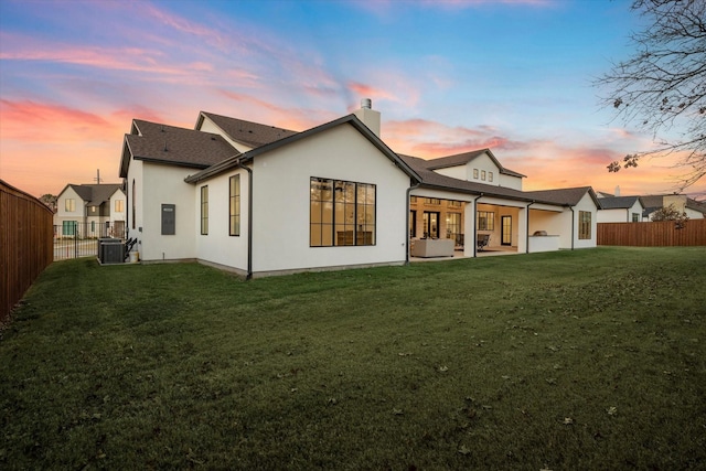 back house at dusk with a lawn, a patio area, and cooling unit