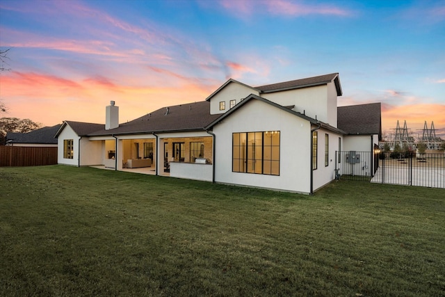 back house at dusk featuring a yard and a patio