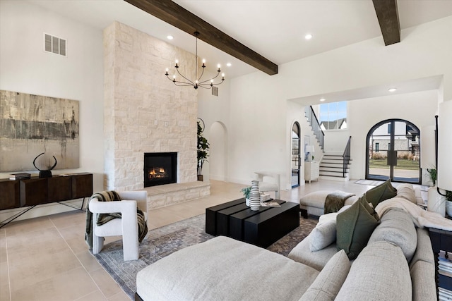 tiled living room with beamed ceiling, a fireplace, a high ceiling, and an inviting chandelier