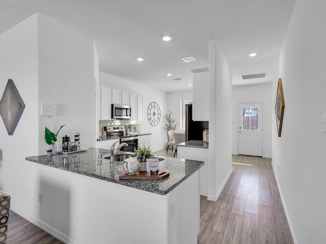 kitchen with white cabinetry, light wood-type flooring, appliances with stainless steel finishes, kitchen peninsula, and dark stone counters