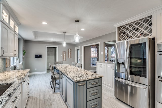 kitchen featuring stainless steel refrigerator with ice dispenser, light stone counters, white cabinets, a center island, and hanging light fixtures