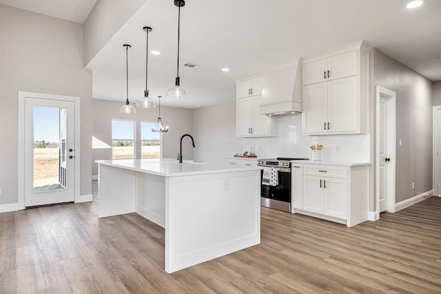 kitchen featuring stainless steel electric stove, white cabinetry, a kitchen island with sink, and custom exhaust hood