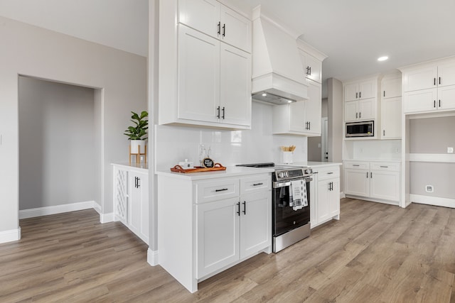 kitchen with white cabinetry, custom range hood, appliances with stainless steel finishes, and light hardwood / wood-style flooring