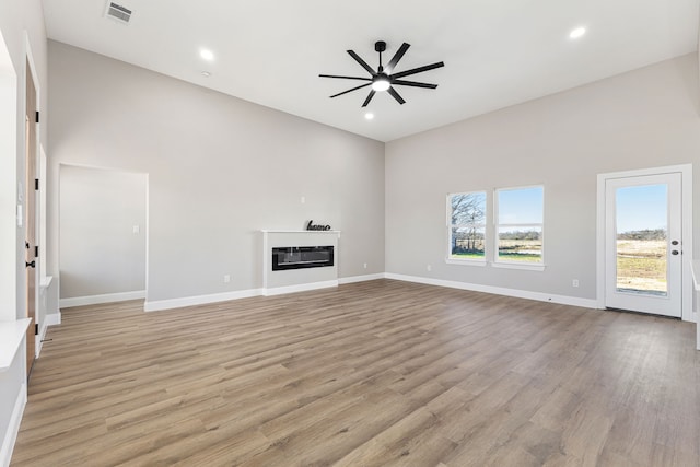 unfurnished living room with a high ceiling, ceiling fan, and light hardwood / wood-style flooring