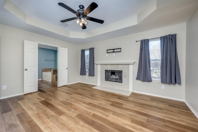 unfurnished living room with hardwood / wood-style floors, ceiling fan, a tile fireplace, and a tray ceiling