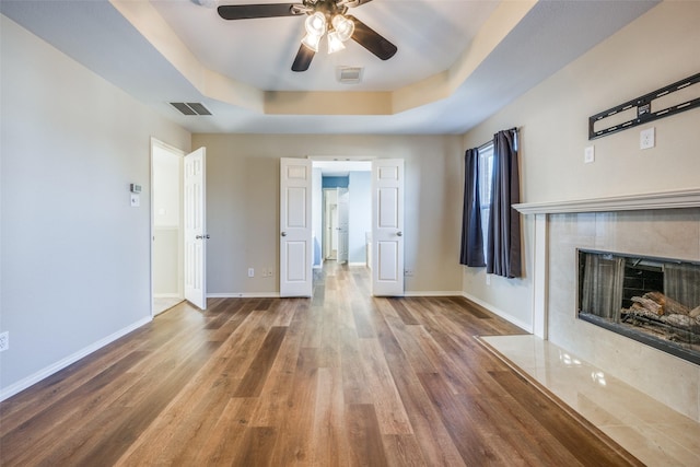 unfurnished living room featuring a fireplace, wood-type flooring, a tray ceiling, and ceiling fan