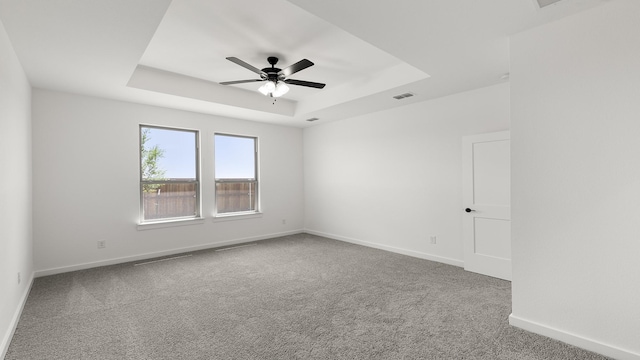 spare room featuring ceiling fan, carpet flooring, baseboards, visible vents, and a tray ceiling