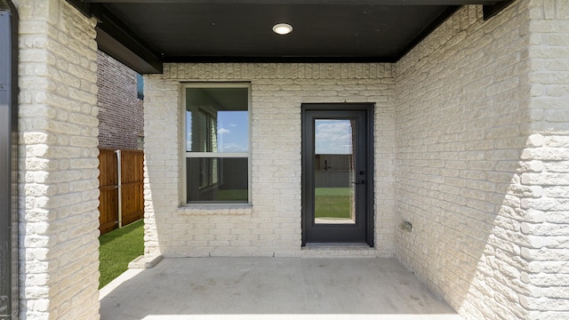 doorway to property featuring brick siding, fence, and a patio area