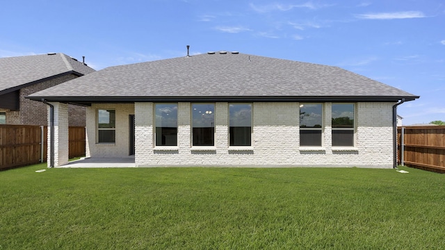 rear view of property with a fenced backyard, a yard, brick siding, a shingled roof, and a patio