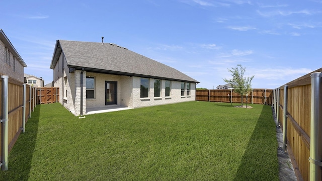 back of house with roof with shingles, a yard, brick siding, and a fenced backyard
