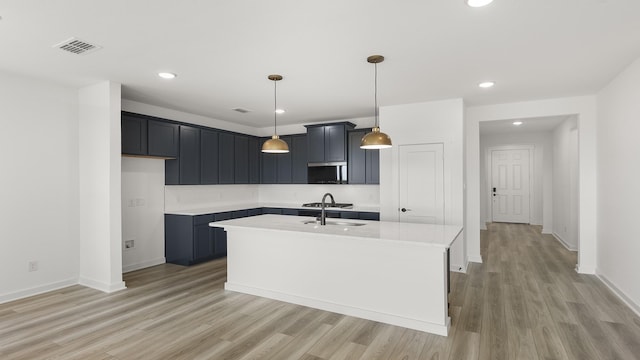 kitchen featuring stainless steel appliances, light countertops, light wood-type flooring, visible vents, and a center island with sink
