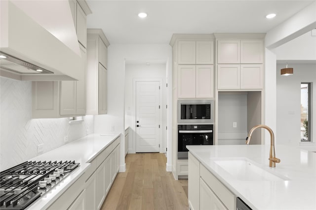 kitchen featuring appliances with stainless steel finishes, sink, white cabinets, light hardwood / wood-style floors, and custom range hood