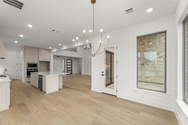 kitchen with pendant lighting, a center island with sink, built in microwave, stainless steel oven, and light wood-type flooring