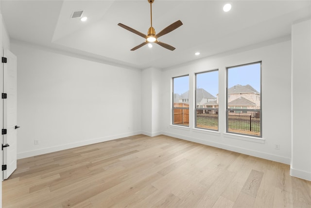 spare room with a tray ceiling, ceiling fan, and light wood-type flooring