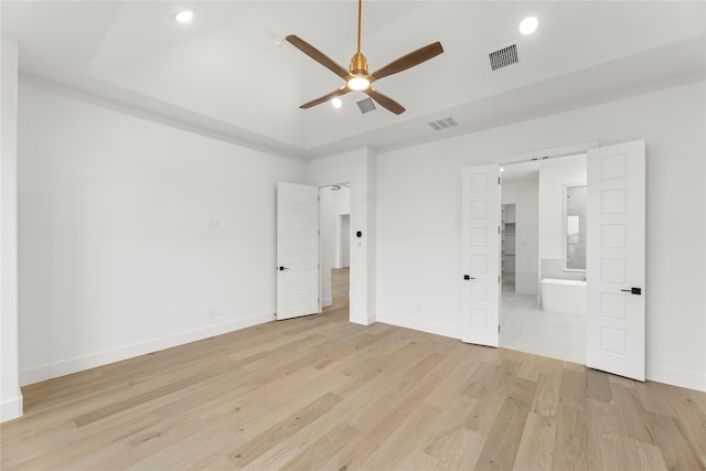 unfurnished bedroom featuring a tray ceiling, light hardwood / wood-style flooring, ceiling fan, and ensuite bathroom