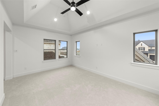 empty room featuring light carpet, vaulted ceiling, a raised ceiling, and ceiling fan