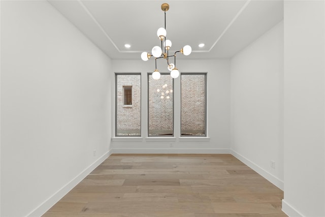 unfurnished dining area featuring a tray ceiling, light hardwood / wood-style floors, and a chandelier