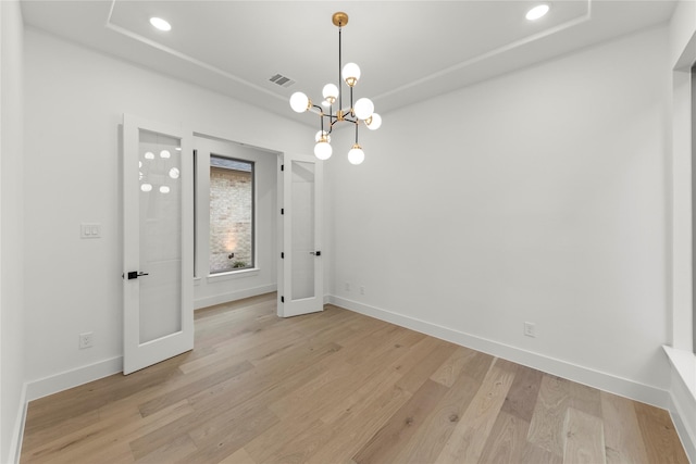 empty room featuring a notable chandelier and light wood-type flooring