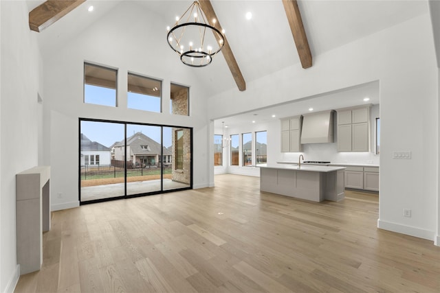 unfurnished living room featuring an inviting chandelier, high vaulted ceiling, beam ceiling, and light hardwood / wood-style floors