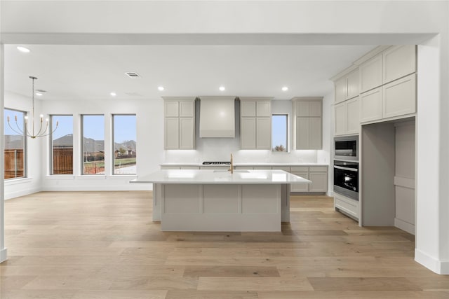 kitchen featuring built in microwave, a center island with sink, stainless steel oven, and wall chimney exhaust hood