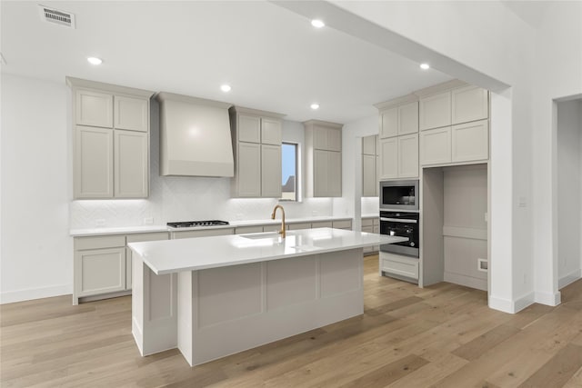 kitchen featuring sink, an island with sink, stainless steel appliances, decorative backsplash, and wall chimney range hood