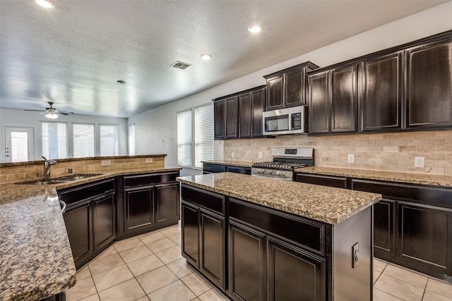 kitchen with backsplash, stainless steel appliances, ceiling fan, sink, and a center island