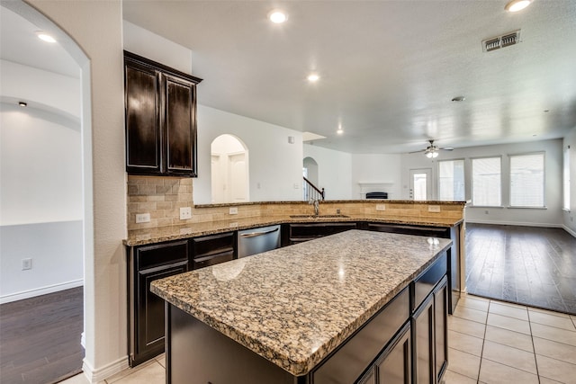 kitchen with a center island, backsplash, ceiling fan, light wood-type flooring, and light stone counters