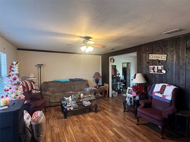 living room with ceiling fan, wooden walls, wood-type flooring, and a textured ceiling