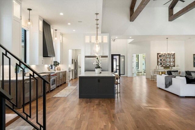 kitchen featuring wall chimney exhaust hood, a kitchen island, high vaulted ceiling, beamed ceiling, and white cabinetry