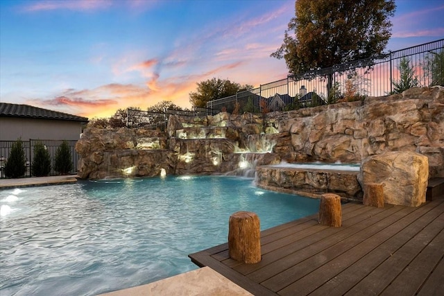 pool at dusk with pool water feature and a wooden deck