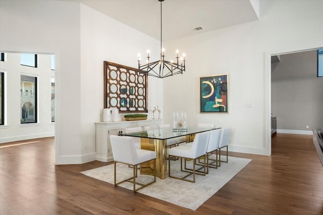 dining room featuring dark hardwood / wood-style flooring, a towering ceiling, and an inviting chandelier