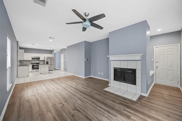 unfurnished living room featuring ceiling fan, a fireplace, sink, and light hardwood / wood-style flooring