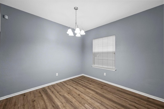 spare room featuring wood-type flooring and a chandelier