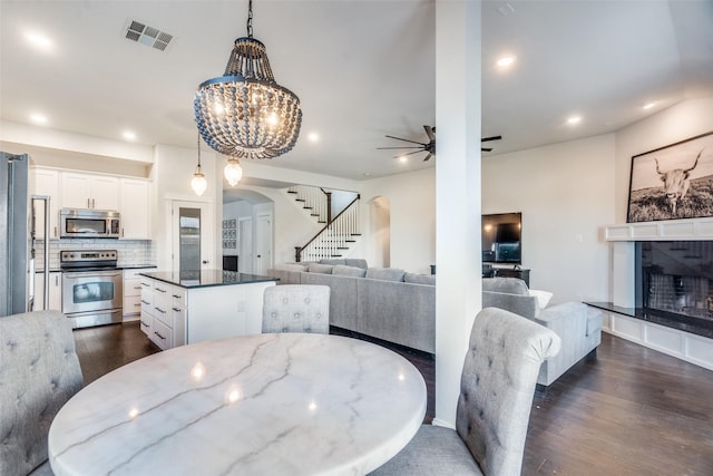 dining space with ceiling fan with notable chandelier, dark hardwood / wood-style flooring, and a tiled fireplace