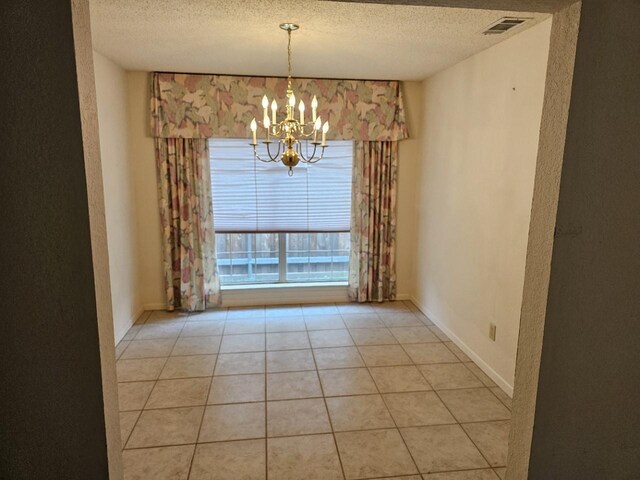 unfurnished dining area featuring light tile patterned floors, a textured ceiling, and an inviting chandelier