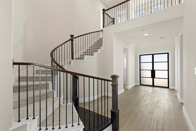 stairs with a towering ceiling, hardwood / wood-style flooring, visible vents, and baseboards