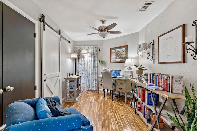 home office featuring ceiling fan, a barn door, wood finished floors, and visible vents