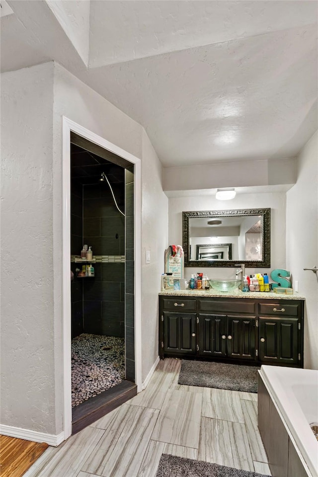 full bath with a relaxing tiled tub, baseboards, a textured wall, vanity, and a shower stall