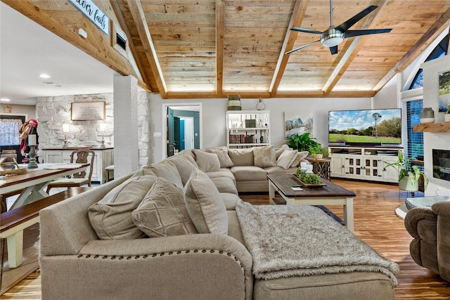 living area with lofted ceiling with beams, a ceiling fan, wood ceiling, a large fireplace, and wood finished floors