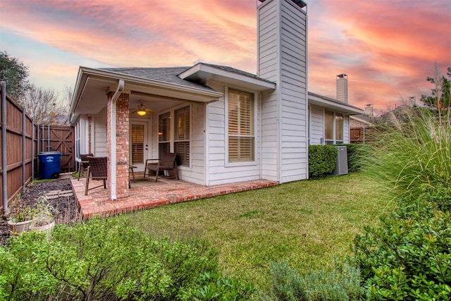 back house at dusk featuring a lawn and a patio area