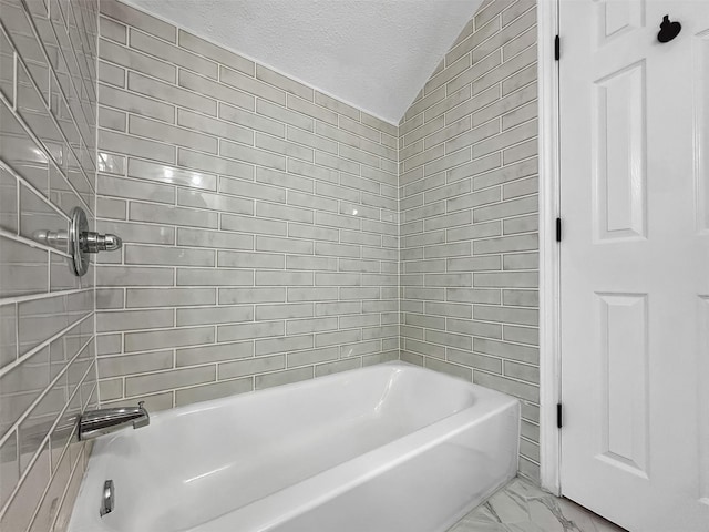 bathroom with a textured ceiling, vaulted ceiling, and tiled shower / bath