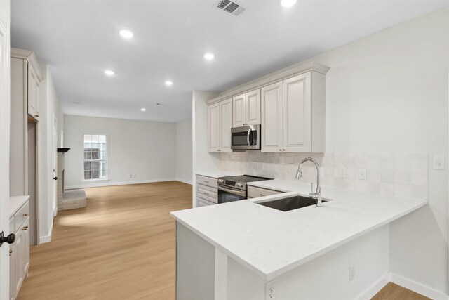 kitchen with kitchen peninsula, appliances with stainless steel finishes, light wood-type flooring, tasteful backsplash, and sink